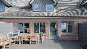 A brick house with a tiled roof, a wooden deck, and a patio table with chairs. - Island idyll Villa Kunterbunt (Fehmarn)