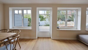A room with three windows, a wooden dining table with chairs, and a grey sofa. - Island idyll Villa Kunterbunt (Fehmarn)