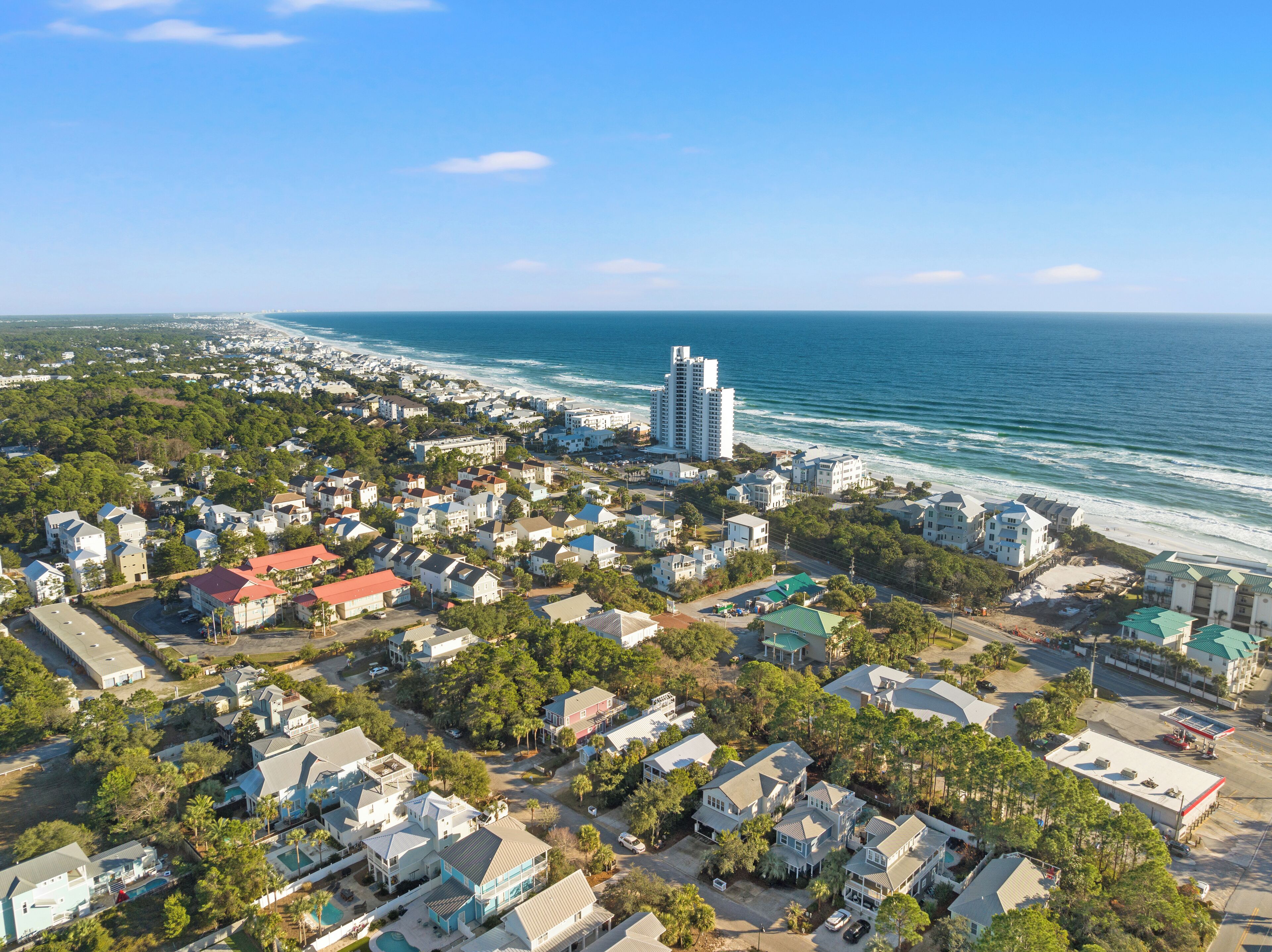 An aerial view of a coastal residential area with houses, a beach, and a gas station.