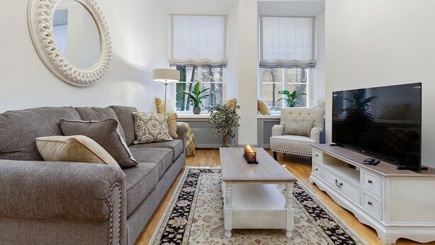 A living room with a grey sofa, a white coffee table, a TV on a white stand, and a large mirror on the wall.