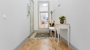 A hallway with a white door, a white chair, a small table with a plant, and a patterned rug.
