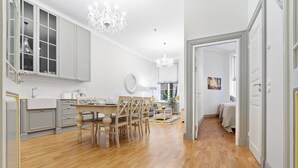 A spacious kitchen with wooden flooring, a dining area with a wooden table and chairs, and a hallway leading to a bedroom.