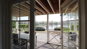 Un espacio al aire libre cubierto con una mesa y sillas, vista a un lago y un área de césped con un banco.