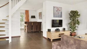 Una sala de estar moderna con una escalera, un comedor, un televisor de pantalla plana y una planta en maceta.