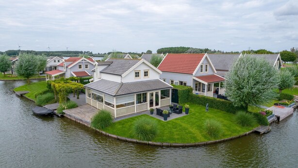 Zona residencial junto al lago con casas de techos rojos y paredes blancas, rodeada de vegetación y una masa de agua tranquila.