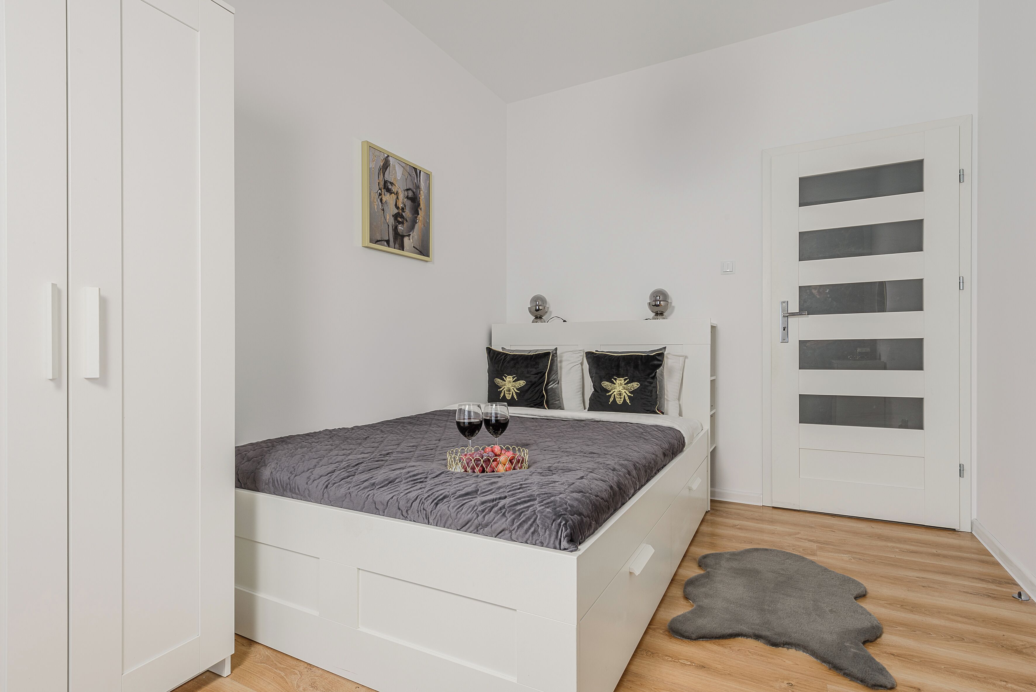Un dormitorio con cama, armario, puerta con paneles de vidrio, alfombra y un cuadro en la pared.