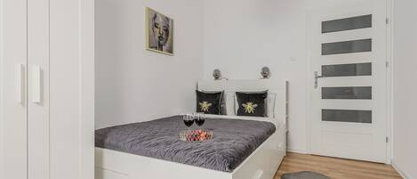 Un dormitorio con cama, armario, puerta con paneles de vidrio, alfombra y un cuadro en la pared.