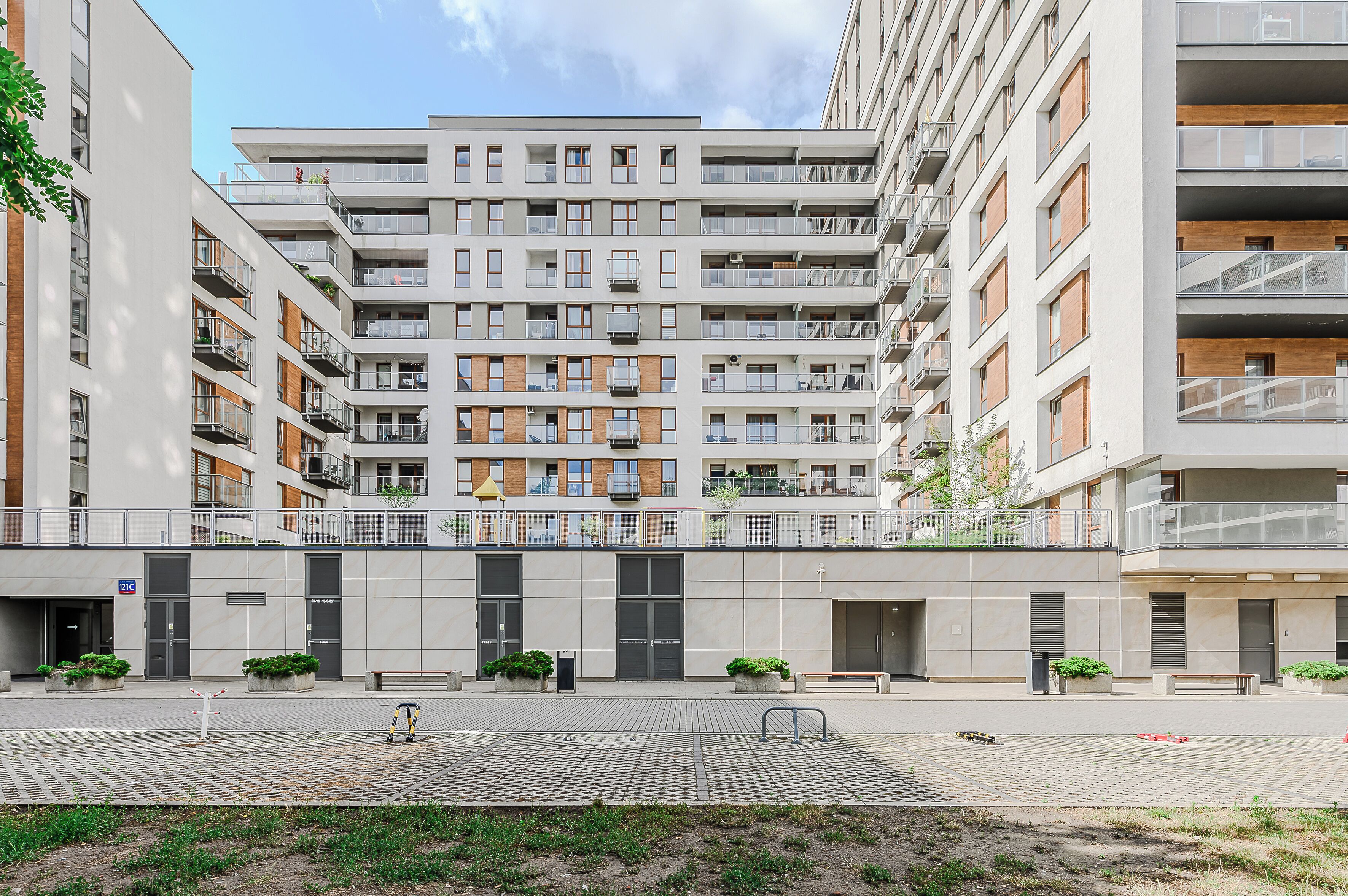 A multi-story residential building with balconies, a paved courtyard, and potted plants.