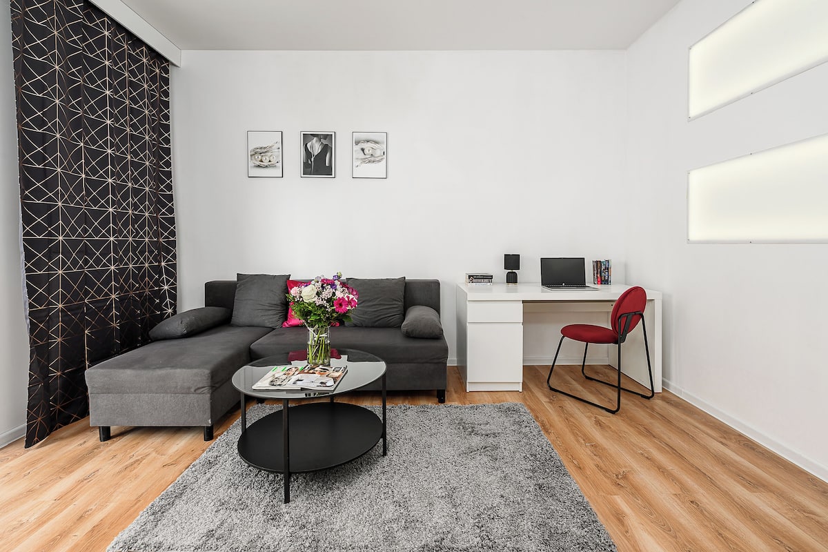 A modern living room with a sectional sofa, a round coffee table, a desk with a computer, and a red chair.