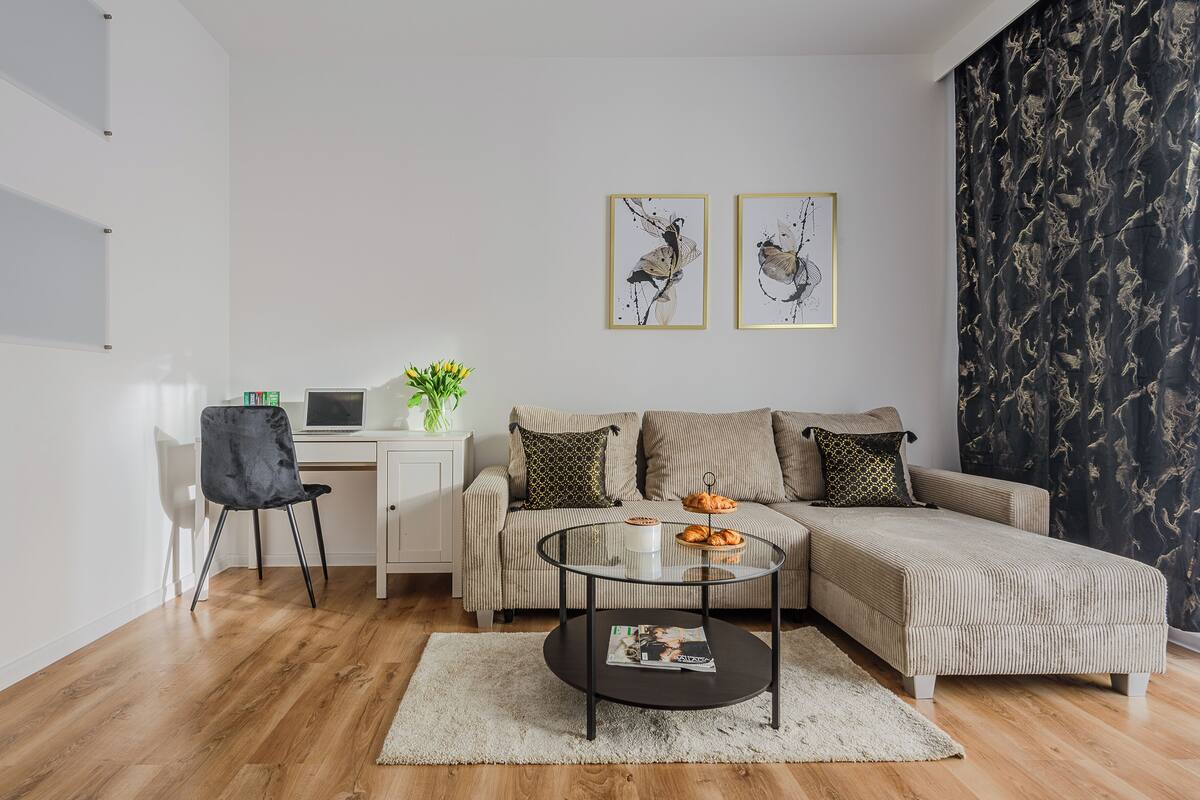 A modern living room with a sofa, a glass coffee table, a desk with a laptop, and two framed artworks on the wall.