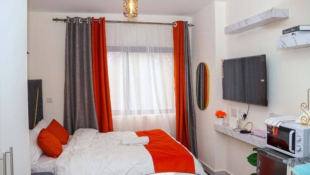 Ein Schlafzimmer mit Bett, Vorhängen, Fernseher, Mikrowelle und einem kleinen Tisch mit Pflanze.