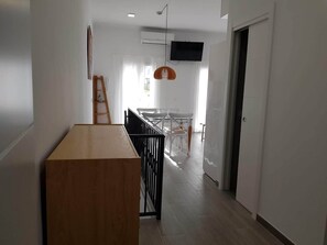 A hallway with a wooden table, a ladder, a TV mounted on the wall, and a dining area with chairs and a table in the background. - Budha's apartment, relax & confort center Calafell (Calafell)