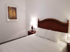 A neatly made bed with white linens, a wooden headboard, and a small bedside table with a lamp. - Budha's apartment, relax & confort center Calafell (Calafell)
