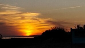 A sunset over a body of water with silhouettes of vegetation and a building in the foreground.