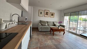 A modern kitchen with a built-in oven, a sink, and a microwave. There is a grey sofa and a wooden coffee table with a vase of flowers. The room has large windows with a view of the outside. - Budha's apartment, relax & confort center Calafell (Calafell)