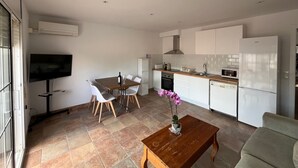 A modern kitchen with white cabinets, a built-in oven, and a microwave. There is a dining area with a table and chairs, and a TV mounted on the wall. - Budha's apartment, relax & confort center Calafell (Calafell)
