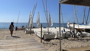 A beach with sailboats docked, a wooden walkway, and a covered area with a bicycle.