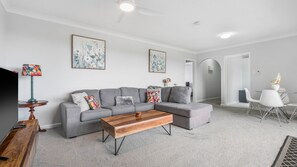 Un salon moderne avec un canapé d’angle gris, une table basse en bois et deux tableaux abstraits accrochés au mur.