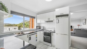 Une cuisine moderne avec des meubles blancs, un four encastré, un four à micro-ondes et un réfrigérateur.