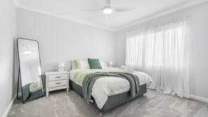 Une chambre à coucher avec un lit, des tables de chevet, un miroir et une fenêtre avec des rideaux légers.