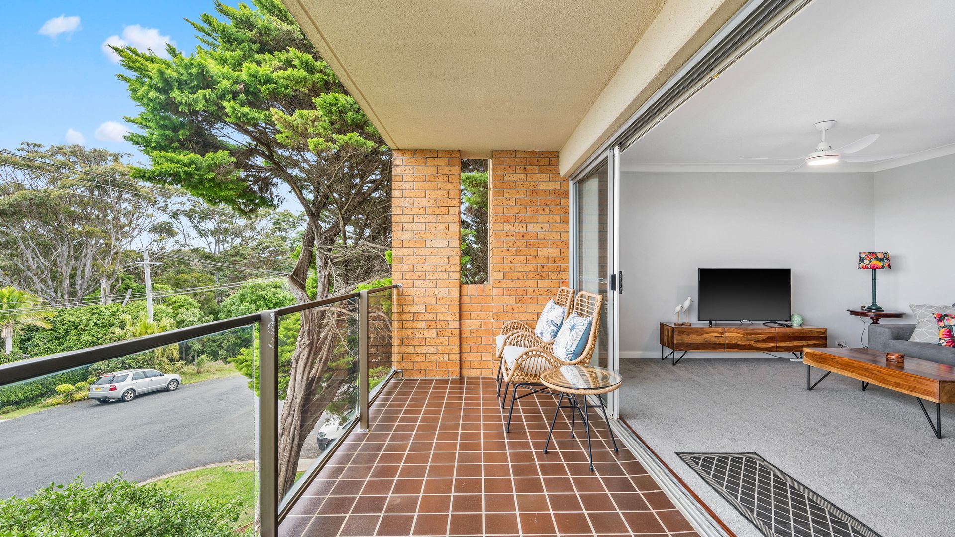 A balcony with a tiled floor, a seating area with chairs, a television, and a decorative lamp.