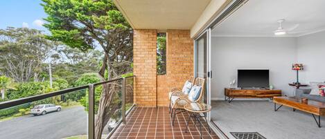 A balcony with a tiled floor, a seating area with chairs, a television, and a decorative lamp.