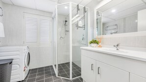Une salle de bain moderne dotée d’une douche à parois de verre, d’un lave-linge encastré et d’un meuble-lavabo avec miroir.
