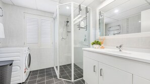 Een moderne badkamer met een douchecabine van glas, een ingebouwde wasmachine en een wastafel met spiegel.