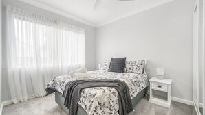 Une chambre à coucher avec un lit, une table de chevet, une lampe et des rideaux légers.