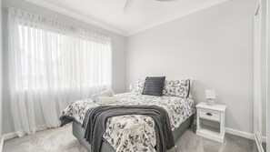 Een slaapkamer met een bed, nachtkastje, lamp en dunne gordijnen.