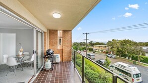 Un balcon doté d’un espace repas, d’une bouteille de gaz et offrant une vue sur une rue animée, avec des voitures et des maisons.