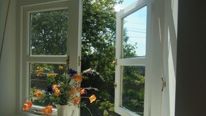 A window with a vase of flowers on the sill, a white door frame, and a view of trees and sky. - Chapel Cottage, spacious light and airy cottage in the Cotswolds AONB (Cirencester)