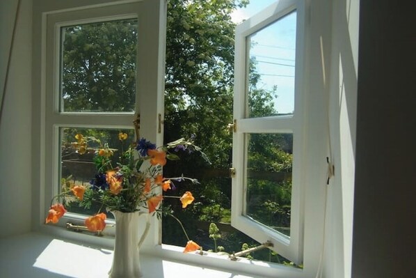 A window with a vase of flowers on the sill, a white door frame, and a view of trees and sky. - Chapel Cottage, spacious light and airy cottage in the Cotswolds AONB (Cirencester)