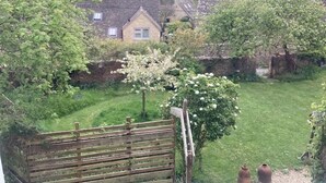 A residential garden with a wooden fence, a white flowering tree, and a house in the background. - Chapel Cottage, spacious light and airy cottage in the Cotswolds AONB (Cirencester)