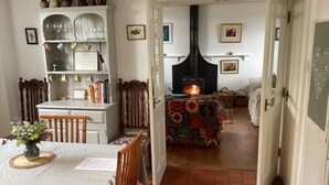 A cozy dining area with a table set for two, a bookshelf, and a fireplace in the background. - Chapel Cottage, spacious light and airy cottage in the Cotswolds AONB (Cirencester)