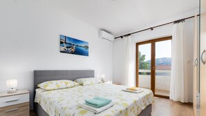 Een slaapkamer met een bed, nachtkastje, raam met gordijnen en uitzicht op de omgeving.