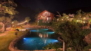 Vista nocturna de un área de piscina con una casa al fondo.