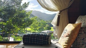 Una cama con vista a un paisaje exuberante tras cortinas translúcidas.