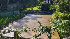 Una casa moderna con terraza de madera, rodeada de exuberante vegetación y una colina.