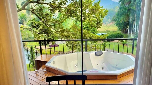 Un balcón con jacuzzi, una mesa con alimentos para el desayuno y una vista panorámica de vegetación y montañas.