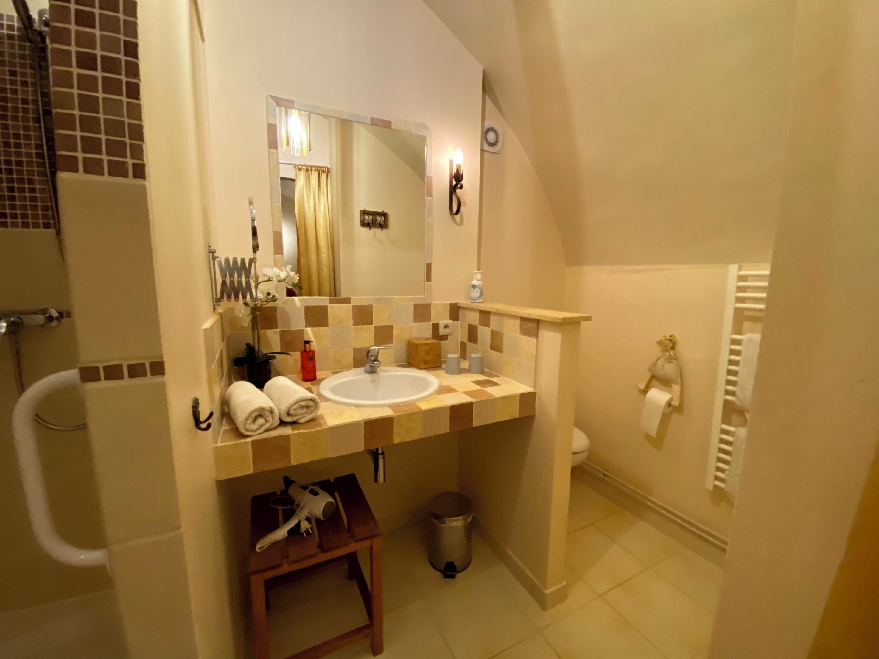 Une salle de bain équipée d’un lavabo, d’un miroir, d’un porte-serviettes et d’une petite table sur laquelle se trouve un sèche-cheveux.