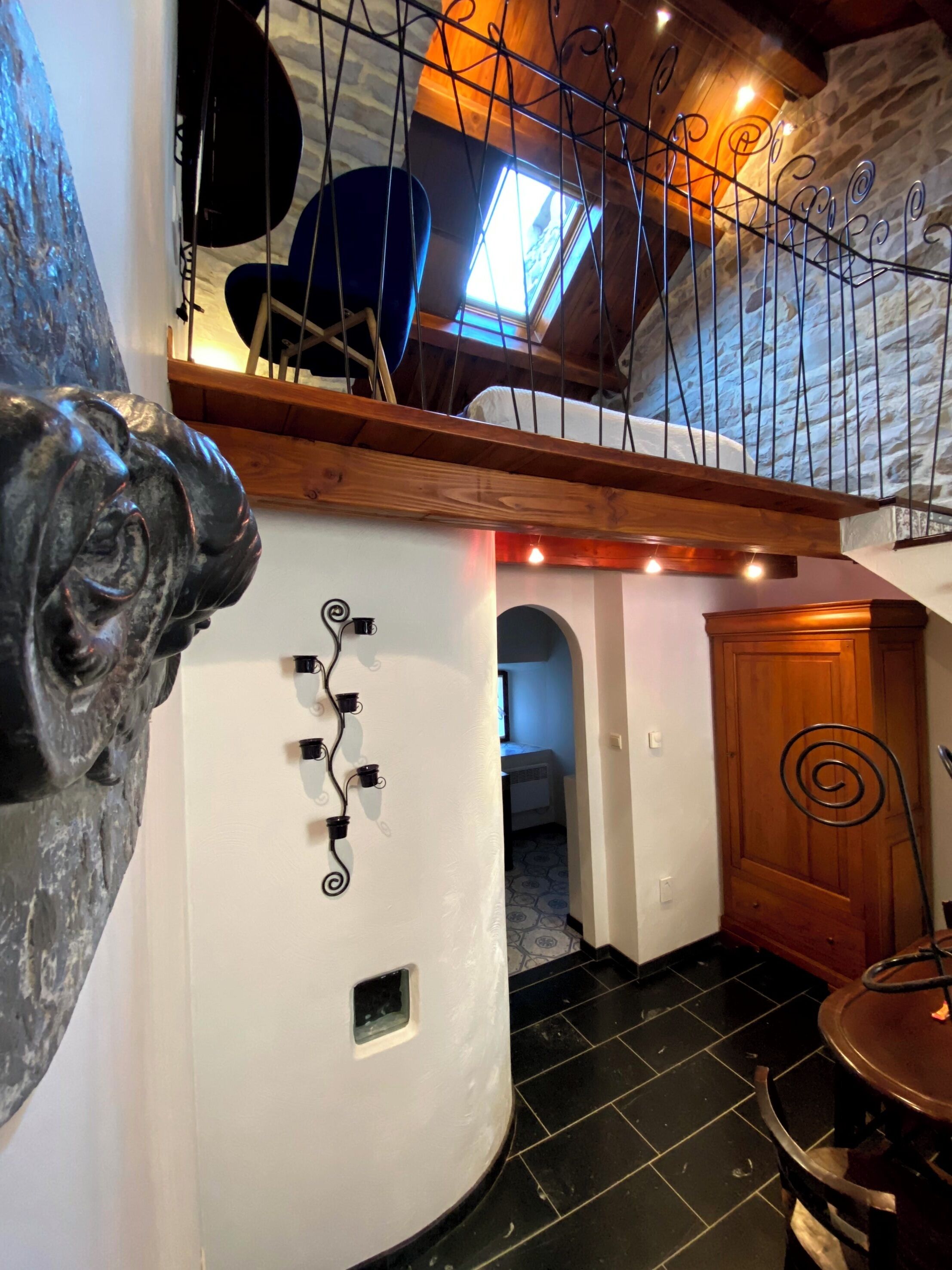 Una habitación con pared blanca curva, suelo de baldosas negras, puerta de madera y decoración metálica en espiral.