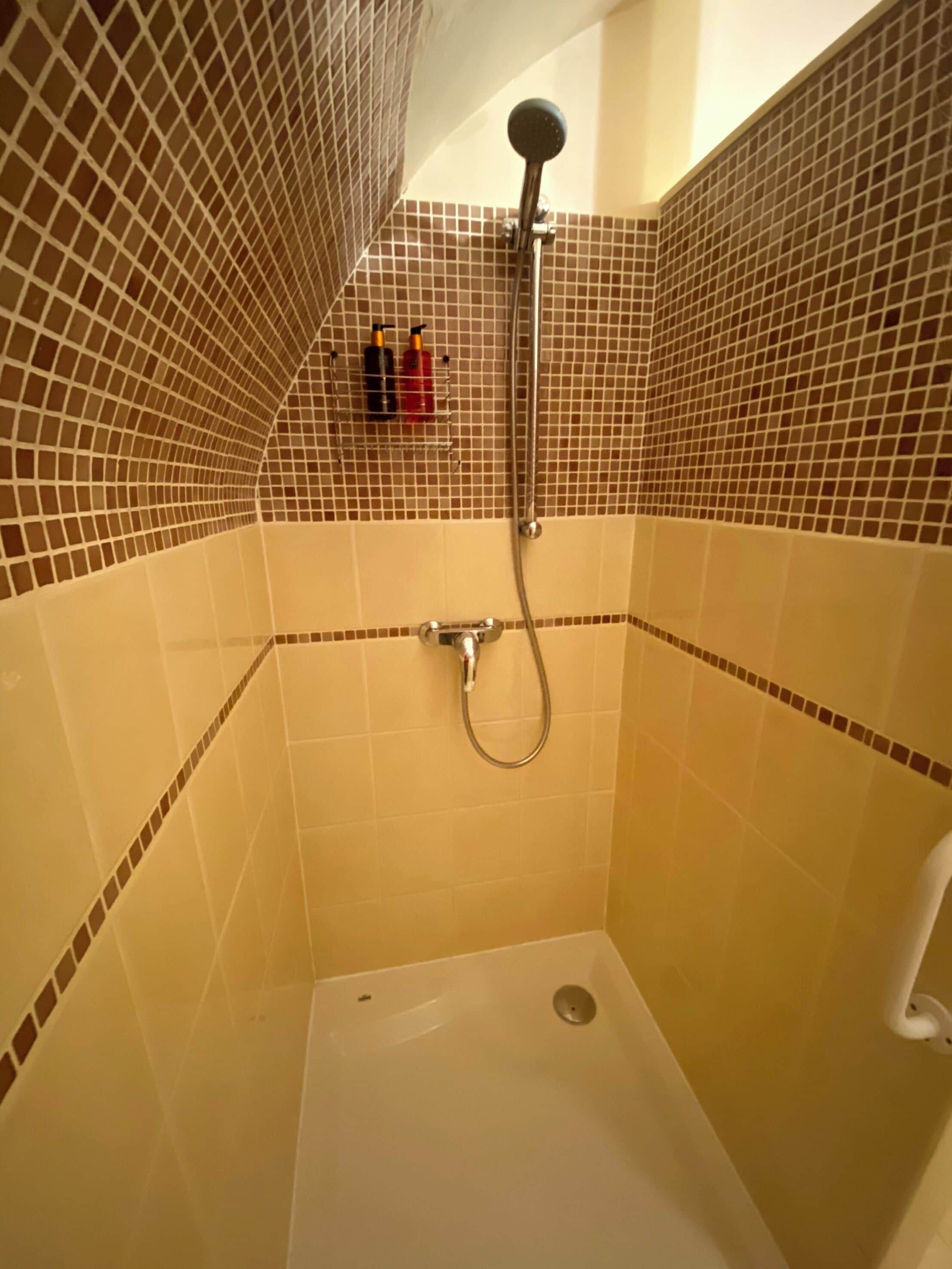 A small, tiled shower room with a handheld showerhead and a wall-mounted faucet.