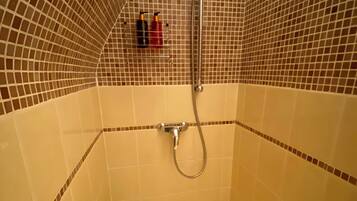 A small, tiled shower room with a handheld showerhead and a wall-mounted faucet.