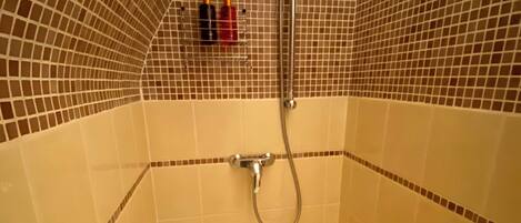 A small, tiled shower room with a handheld showerhead and a wall-mounted faucet.