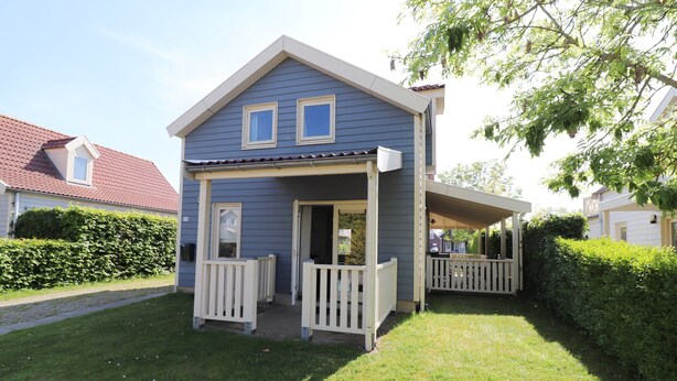 A two-story house with a porch, a small deck, and a well-maintained lawn. - Bungalow by Water With Sauna in South Holland (Simonshaven)