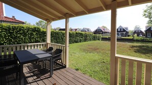 A covered outdoor area with a table and chairs, a wooden deck, and a view of houses in the background. - Bungalow by Water With Sauna in South Holland (Simonshaven)