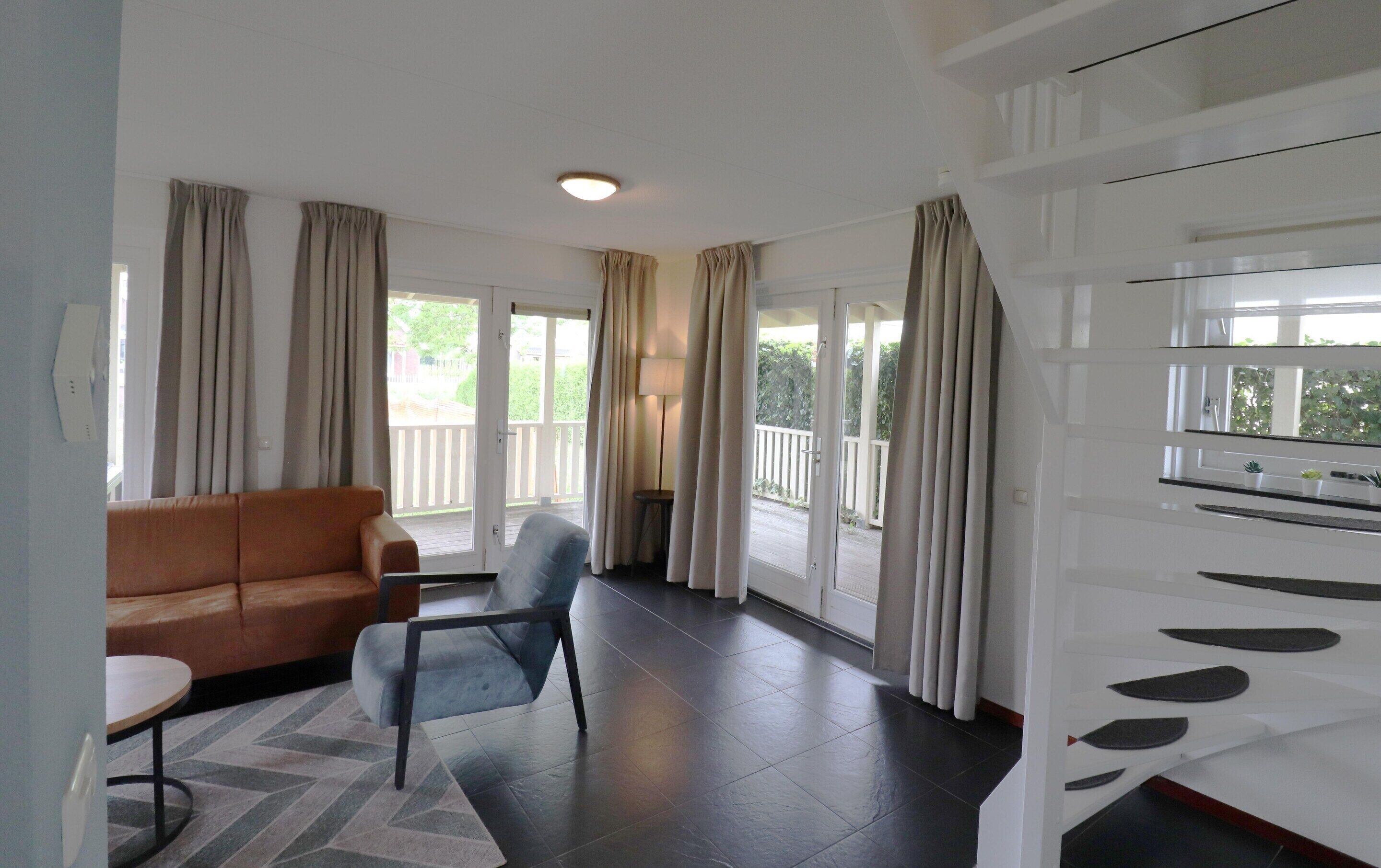 A living room with a sofa, a chair, a table, and a large window with curtains.