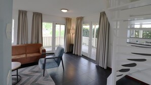 A living room with a sofa, a chair, a table, and a large window with curtains. - Bungalow by Water With Sauna in South Holland (Simonshaven)