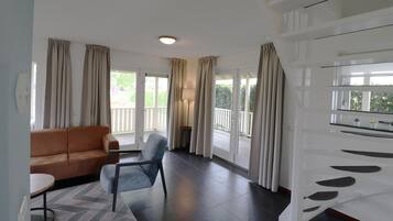 A living room with a sofa, a chair, a table, and a large window with curtains.